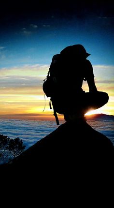 the silhouette of a person with a backpack on top of a mountain at sunset or dawn