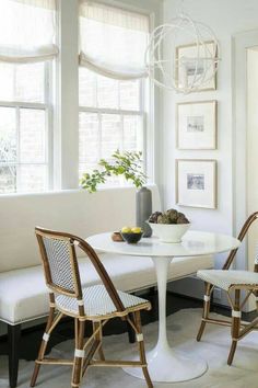 a white table with two chairs and a bowl of fruit on it next to a window