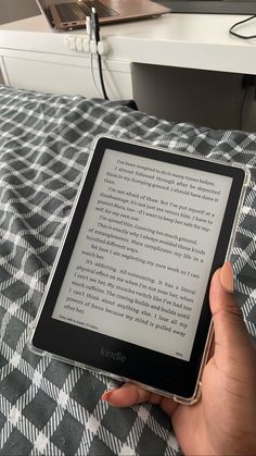 a person is holding an electronic device in their hand while sitting on a bed with a checkered blanket