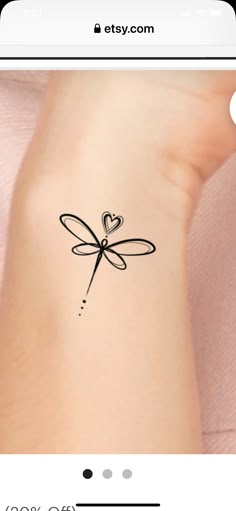 a small tattoo on the wrist of a woman with a heart shaped dragonfly attached to it