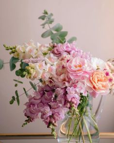 a vase filled with pink and white flowers sitting on top of a wooden table next to a mirror