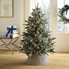 a small christmas tree in a basket on the floor next to a window with blue and white decorations