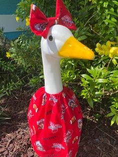 a plastic duck wearing a red dress in front of some bushes