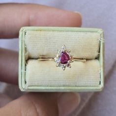 a person holding a ring with a red stone in it's center and diamond accents on the band