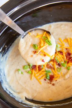 a spoon full of soup with cheese and green onions on the side in a crock pot