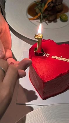 a person lighting a candle on top of a heart shaped cake