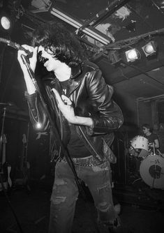 black and white photograph of a man singing into a microphone while holding a guitar in front of him