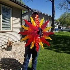 a man standing in front of a house holding a red and yellow flower shaped object