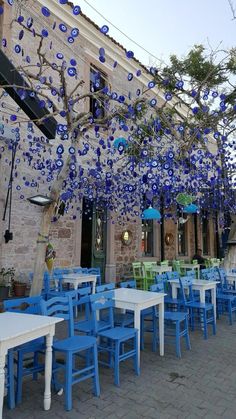 an outdoor dining area with blue and green chairs, tables and umbrellas hanging from the ceiling