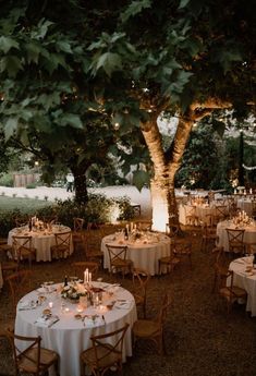 an outdoor dining area with round tables and white tablecloths set up under a tree