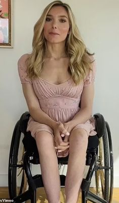 a woman in a pink dress sitting on a wheel chair with her legs crossed and looking off to the side