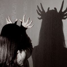 the shadow of a woman's head and hands against a wall with deer antlers on it