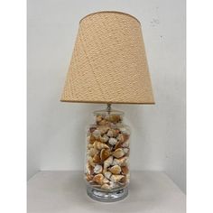 a lamp that is on top of a table with shells in the jar underneath it