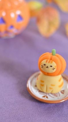 an orange and white cat figurine sitting on top of a purple table cloth