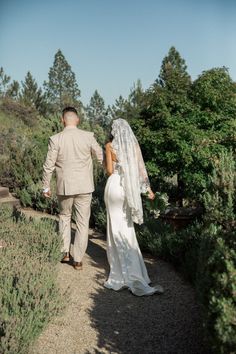 a bride and groom walking down a path in front of some bushes on their wedding day