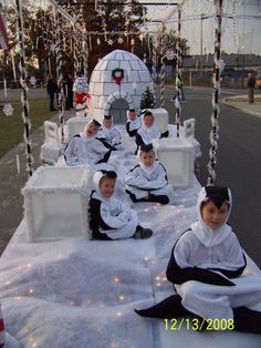 several children dressed in costumes sitting on ice blocks with lights strung from the sides and around them