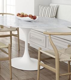 a white table and chairs in a room with wood flooring on one side and a bowl of fruit on the other