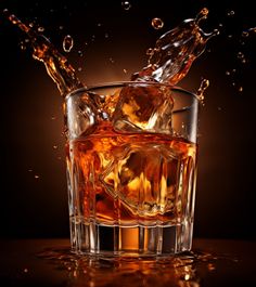 ice cubes splashing into a glass of whiskey on a dark background with reflections