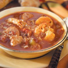 a bowl of soup with meat and vegetables on a plate next to some bread rolls