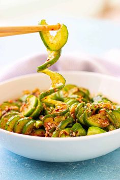 a white bowl filled with green vegetables and chopsticks sticking out of the top