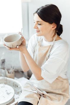 a woman in an apron is holding a bowl and spoon while sitting on the kitchen counter