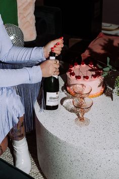 a woman sitting at a table with a cake and wine bottle in front of her