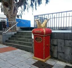 a red mailbox sitting on the side of a street next to stairs and a tree