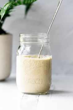 a glass jar filled with dressing next to a potted plant