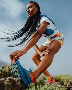 a woman with long hair crouching down on the ground while holding onto her running shoe