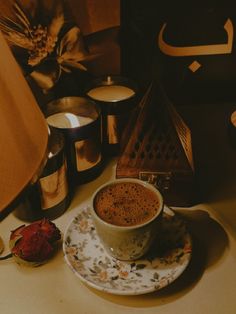 a cup of coffee sitting on top of a saucer next to candles and a lamp