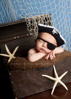 a baby wearing a pirate hat laying on top of a wooden trunk next to starfish