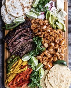 a wooden platter filled with meat, veggies and tortilla shells