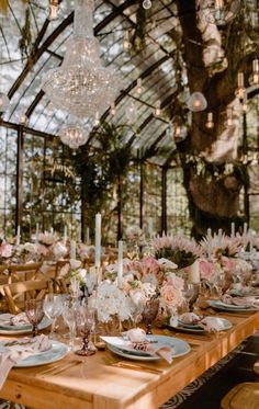 a table set with flowers and candles for a wedding reception in a glass walled room