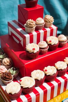 a red and white striped cake with cupcakes on the top is stacked high