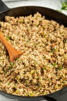 a skillet filled with rice and vegetables on top of a table next to a wooden spoon