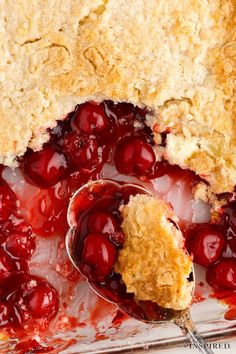 a close up of a pie with cherries on it and a spoon in it