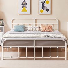 a white metal bed in a bedroom with two pictures on the wall above it and an end table next to it