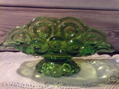 a green glass bowl sitting on top of a white doily covered table cloth next to a wooden wall