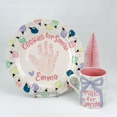 a pink christmas tree sits next to a ceramic plate and mug with handprints on it