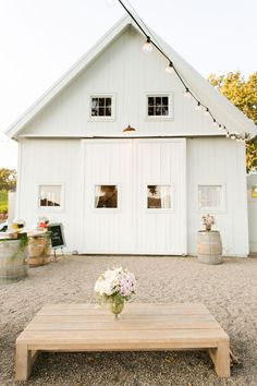 a wooden table sitting in front of a white barn