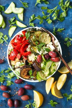 a bowl filled with vegetables next to sliced lemons and olives on a blue surface