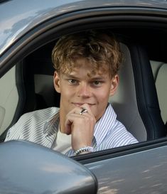 a young man sitting in the driver's seat of a car with his hand on his chin