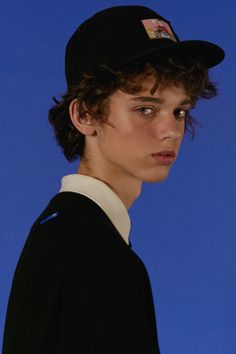 a young man with curly hair wearing a black hat