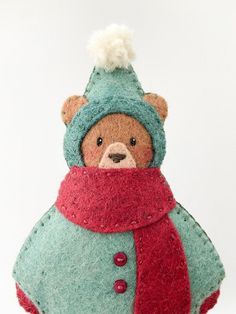 a teddy bear wearing a blue coat and red scarf with a pompom on its head