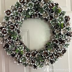 a wreath made out of pine cones and green leaves is hanging on the front door