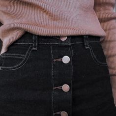 a woman wearing a pink sweater and black skirt with buttons on the bottom of her pants