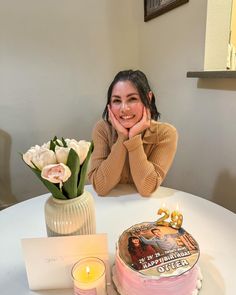 a woman sitting at a table with a birthday cake and flowers in front of her