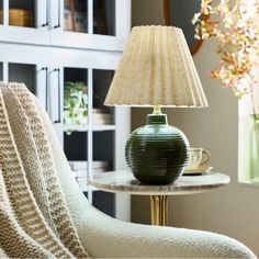 a green lamp sitting on top of a table next to a chair and bookcase