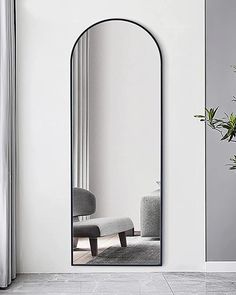 a large mirror sitting on top of a white wall next to a chair and potted plant