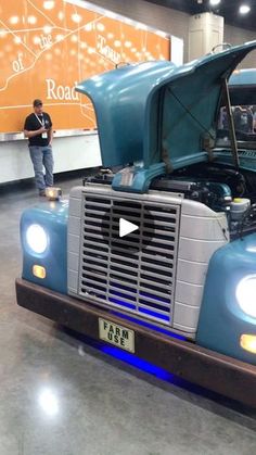 a man standing next to a blue truck with its hood up and the engine open